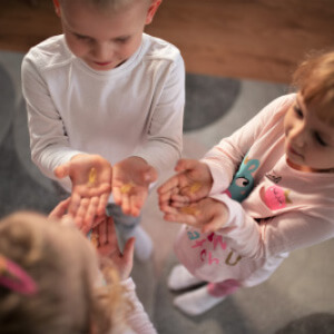 Natural Pharmaceuticals OmegaMarine Junior+ Lapsed seisavad ringis ja vaatavad avatud peopesadesse, hoides väikseid kollaseid esemeid.