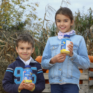 Natural Pharmaceuticals OmegaMarine Junior+ Kaks last hoiavad õues vitamiinipurke, taustal sügisene aiamaa ja kõrvitsad.